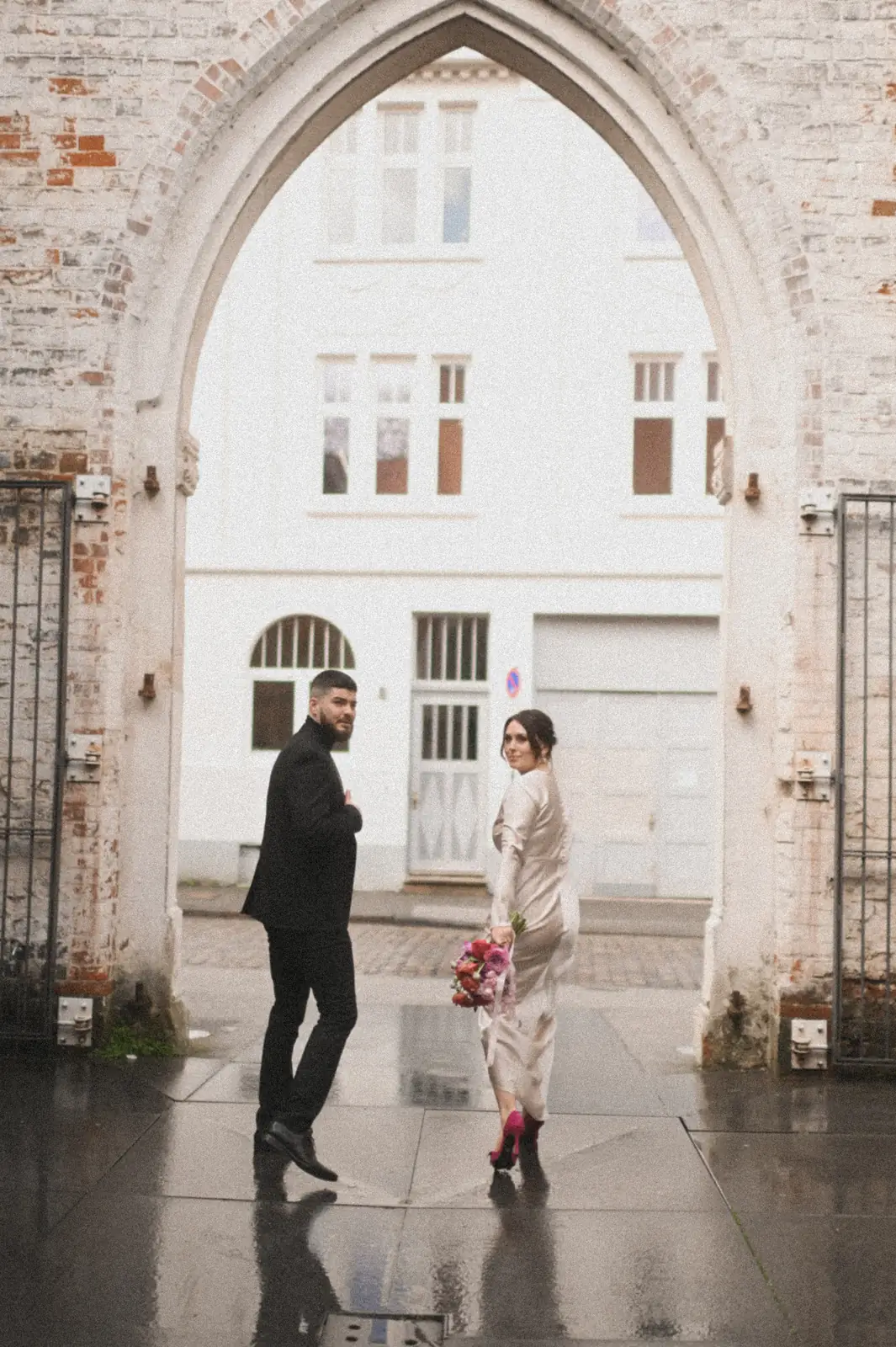 Das Paar geht durch einen Torbogen aus Backstein auf nassem Kopfsteinpflaster