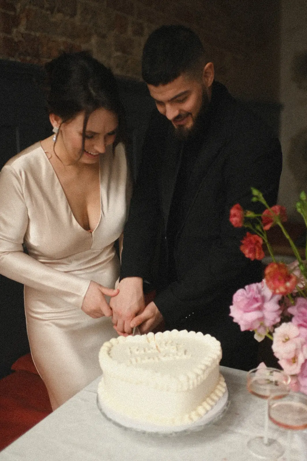 Das Paar schneidet gemeinsam eine weiße Torte an, daneben Blumen in Pink und Rot